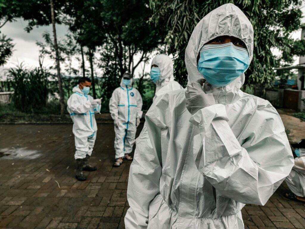 People in white protective suits and blue face masks standing on a paved area